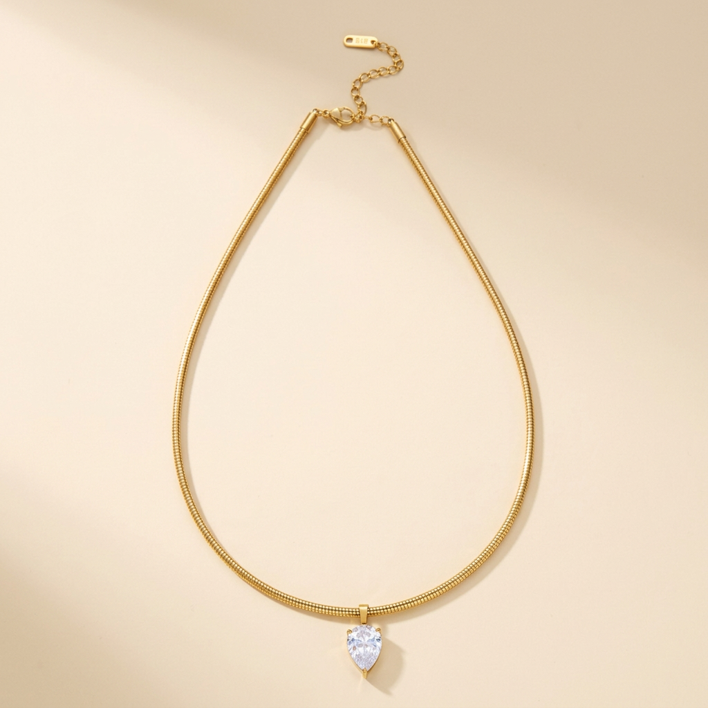 Gold-tone snake chain choker with clear teardrop pendant on ivory