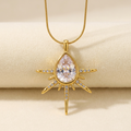 Gold-tone sunburst teardrop pendant necklace against an ivory background