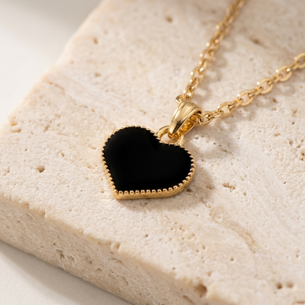 Black enamel heart with beaded gold-tone border on travertine